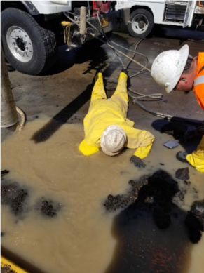 Worker reaching down, shoulder deep in a muddy pool of water to shut off valve.